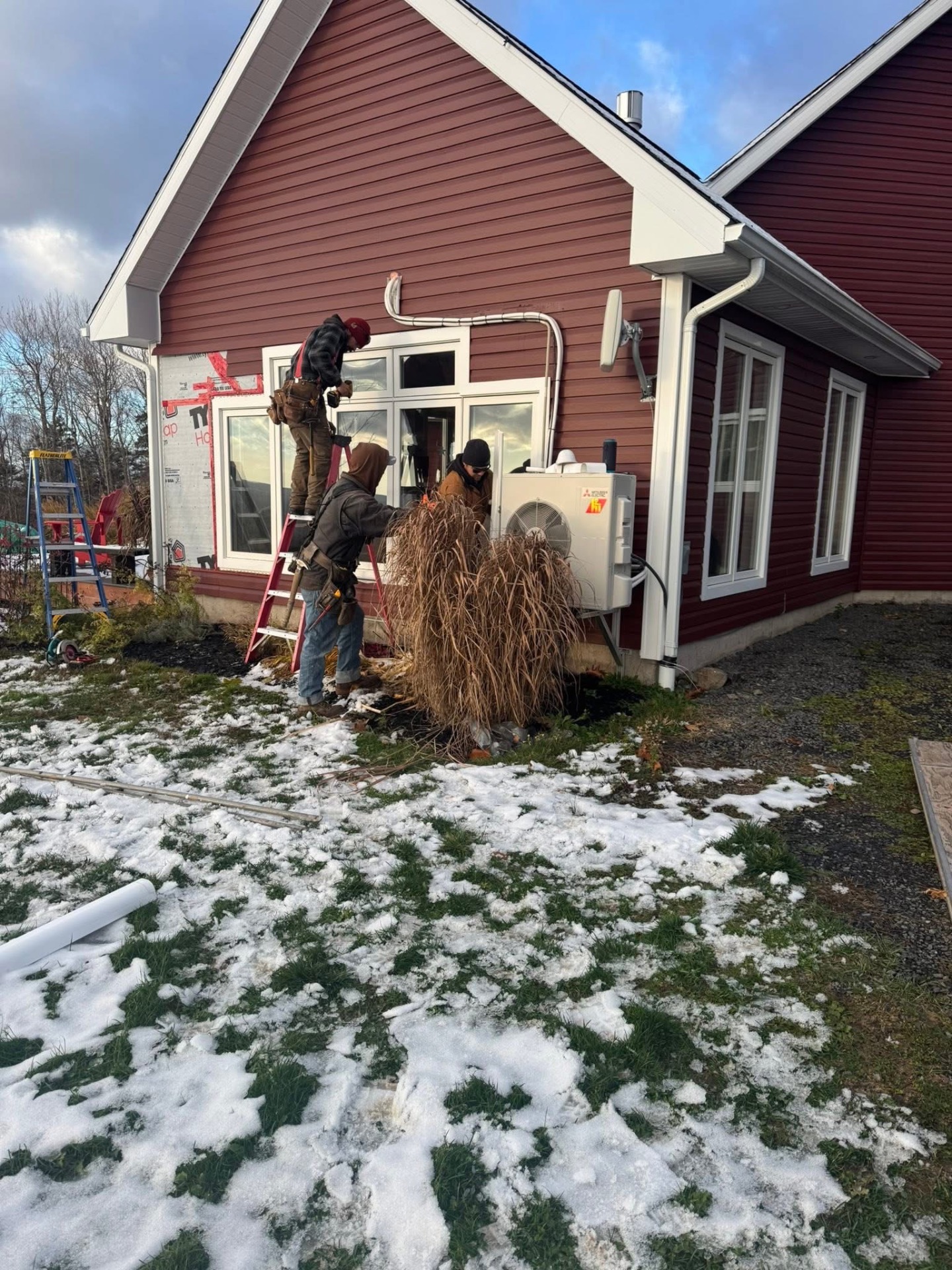 Crew installing large windows on a red-sided home in winter