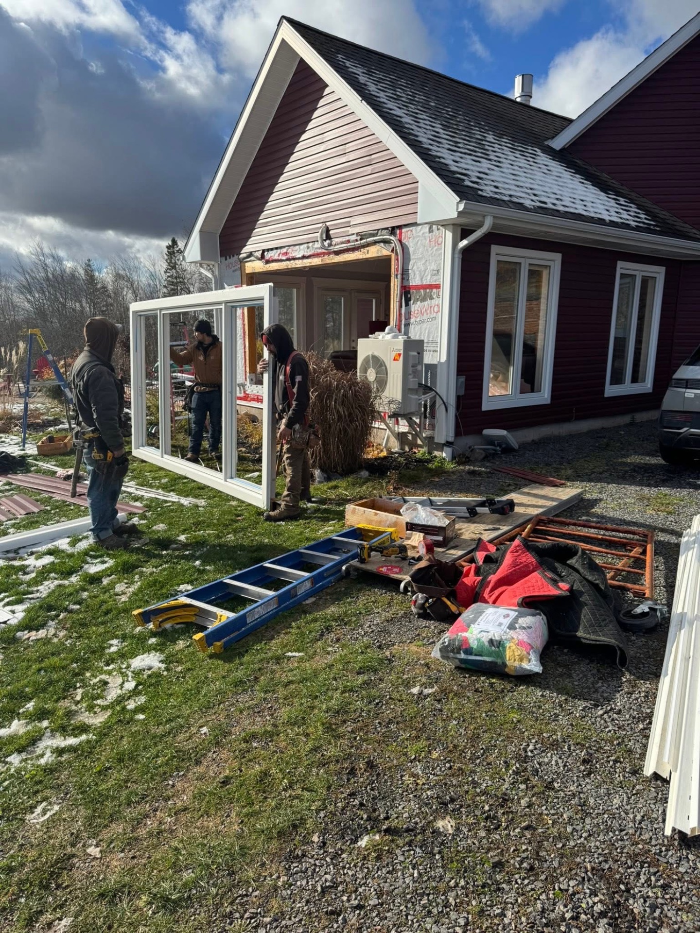 Crew carrying a new window to a red home during installation
